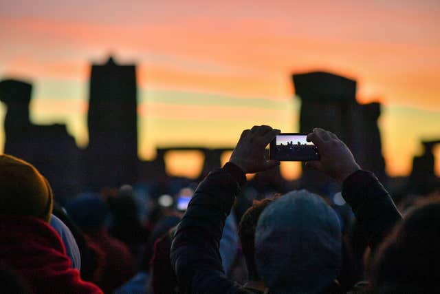 The sun breaks the horizon and shines through the stones at Stonehenge onto crowds of people celebrating the dawn of the longest day in the UK (Ben Birchall/PA)