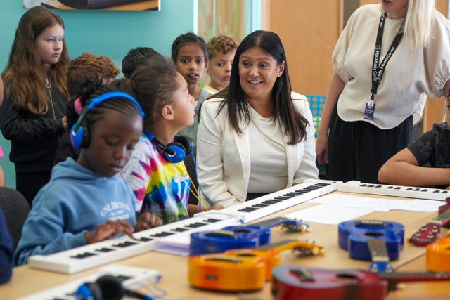 Lisa Nandy talking to children as she sits with them around a table with various musical instruments on it