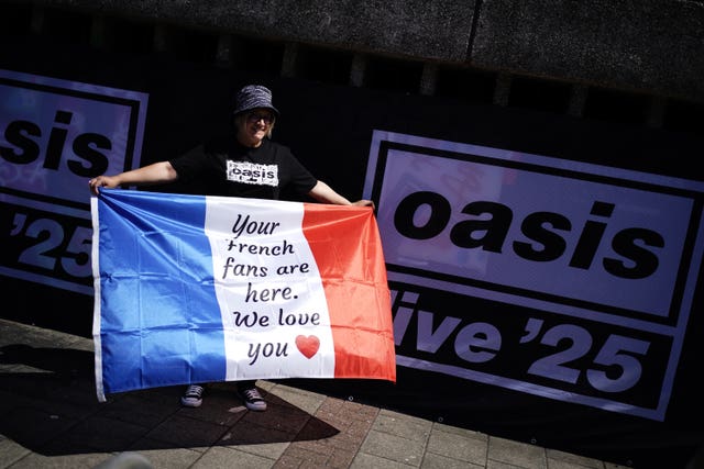 An Oasis fan holding a French flag poses for a photo outside the Principality Stadium