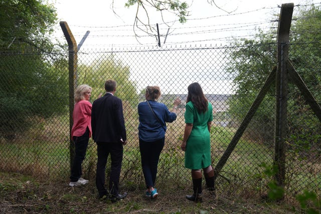 Shadow home secretary Chris Philp, shadow minister for women and equalities Joy Morrissey (right) and residents of Piddington look through the wire fence at the former military base