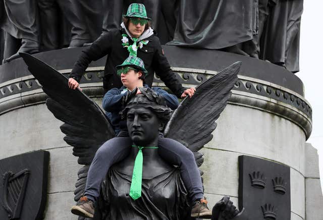 Spectators sit on the O’Connell monument to watch the parade (Brian Lawless/PA)