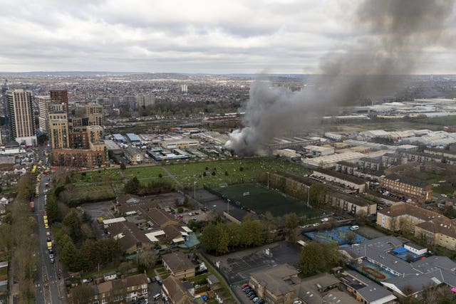 Emergency vehicles line the road as smoke rises over the fire