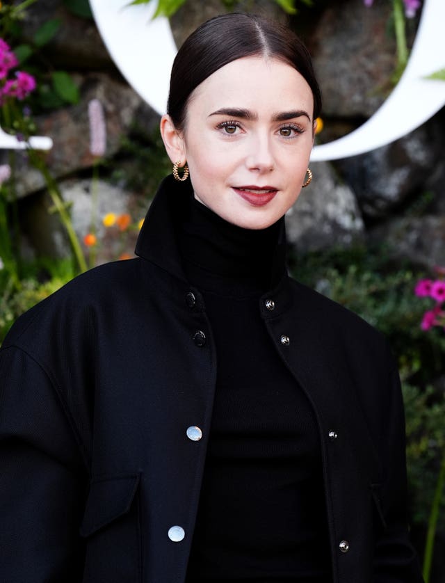 Lily Collins with her hair in a bun and wearing a high neck black coat
