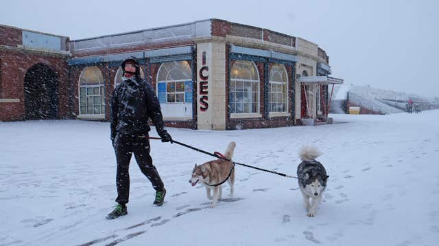 A man walks with his dogs in heavy snow at Whitley Bay beach