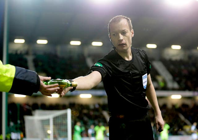 Referee Willie Collum removes a bottle from the Easter Road pitch after it was thrown at Celtic winger Scott Sinclair