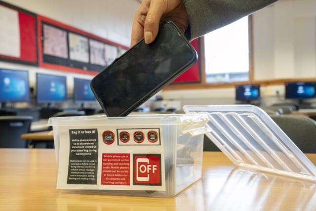A student placing a mobile phone in a box before the start of a lesson