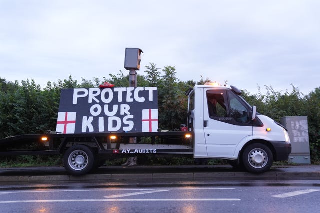 A flat bed truck parked on the side of a road holds a sign that reads 'protect our kids'