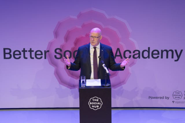 John Swinney speaking from a podium, with a background which reads 'Better Society Academy'