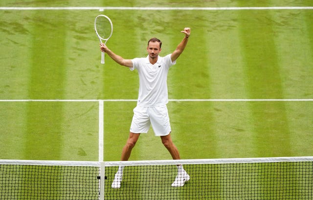 Daniil Medvedev raises his arms and racket aloft in celebration in front of the net