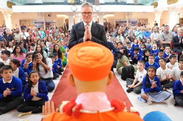 Sir Keir Starmer clasps his hands together in front of his chest, with children behind him