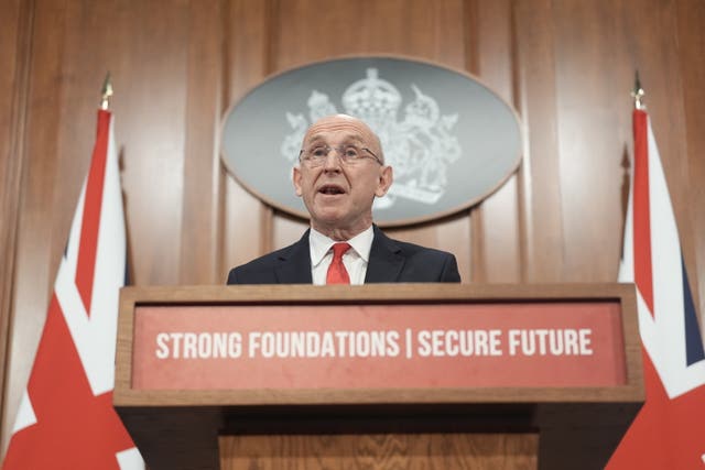 John Healey delivering a speech from a lectern which says 'Strong foundations. Secure future'