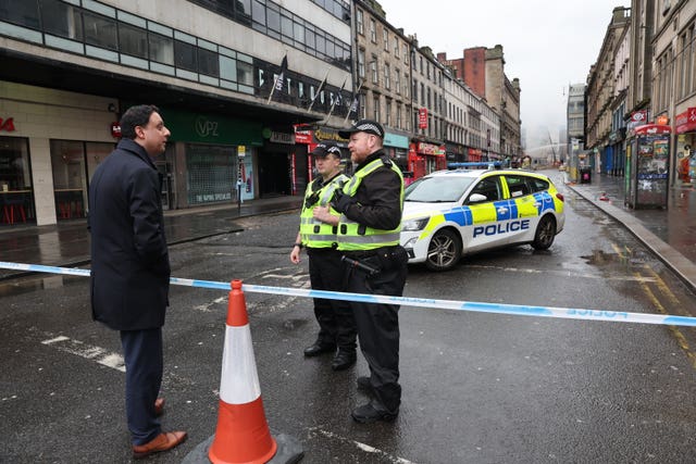 Anas Sarwar speaking to two police officers on the other side of police tape cordoning off the scene of the fire