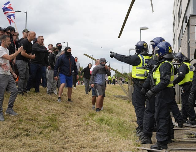 Ricky Hardman (left, bald head, black top and grey cargo trousers) standing with a group of men as objects are thrown towards police at the Holiday Inn Express in Rotherham, South Yorkshire