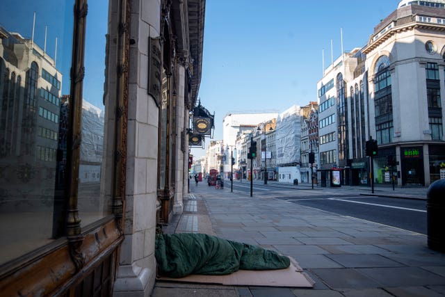 A homeless person lies on the pavement during rush hour on the Strand in Westminster, London (Victoria Jones/PA)