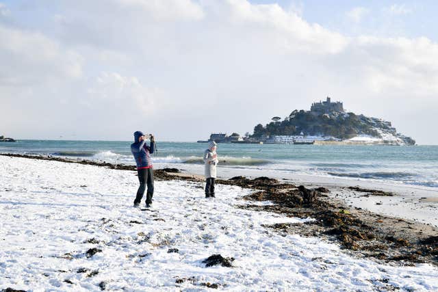 People stand on the snow-covered Marazion beach, with St Michael's Mount in the background, in Cornwall, (Ben Birchall/PA)