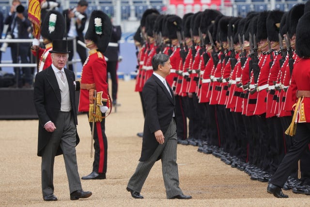 The King follows behind as Emperor Naruhito inspects soldiers in red uniforms and bearskin hats