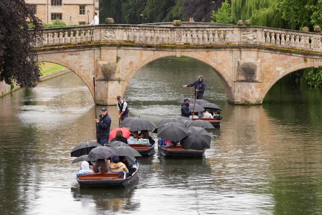 People shelter from rain under umbrellas as they punt along the River Cam in Cambridge