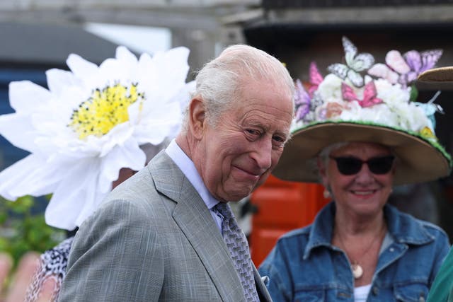 The King smiling, with women in the background wearing large floral hats