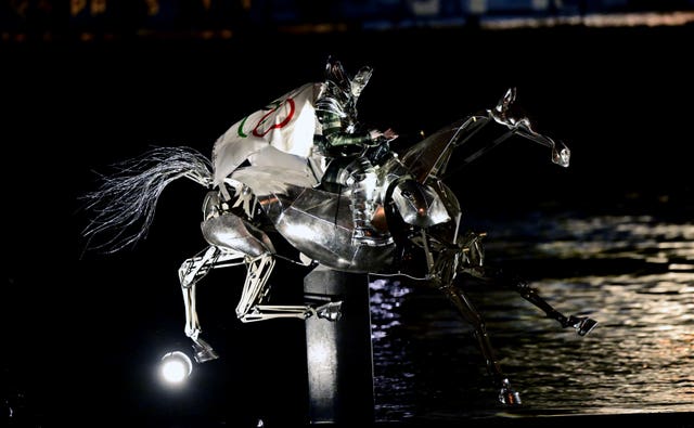 A horsewoman, wearing the flag of the IOC rides a metal horse down the Seine