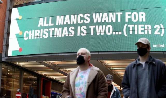 People wearing face masks walk past a sign on Market Street, Manchester
