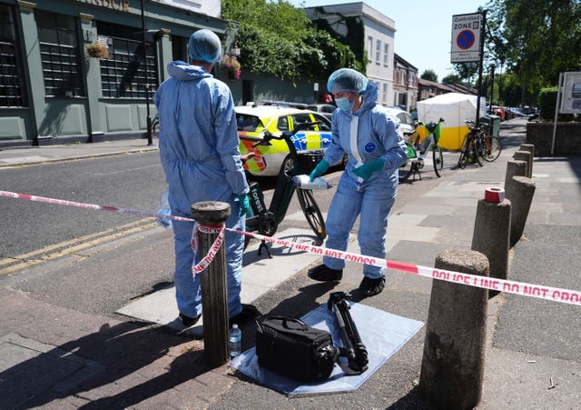 Officers in forensic suits lay out equipment at the scene outside Lopez House on Willington Road in Clapham, south London, after a 25-year-old man was shot dead on Monday evening