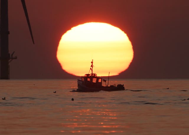 A fishing boat sails in front of the rising sun near Blyth pier in Northumberland