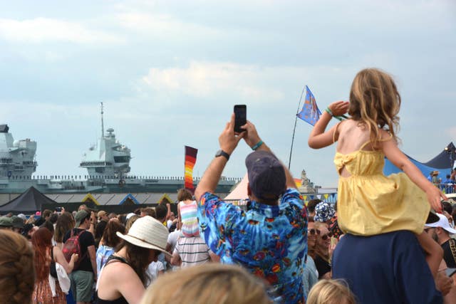 Festival goers at the Victorious Festival on Southsea Common give Royal Navy aircraft carrier HMS Prince of Wales a colourful send-off