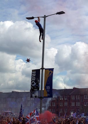 A Rangers fan clings on to a lamp post outside Ibrox