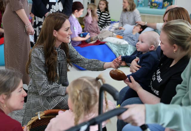 Princess of Wales holding hands with a young child who is in the arms of their mother