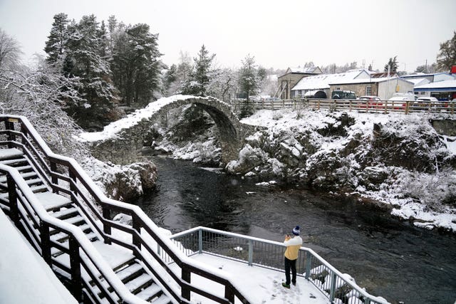 A person takes photographs of snow on an arch in Carrbridge in the Scottish Highlands