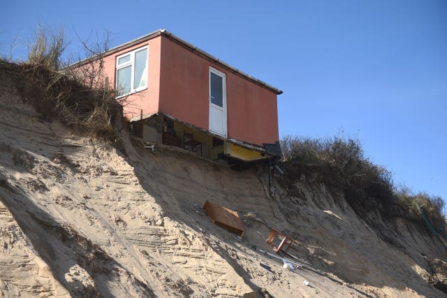 A partially-collapsed house sits on the cliff edge at The Marrams in Hemsby (Joe Giddens/PA)