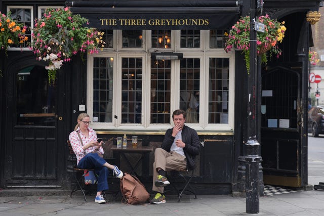 A person smokes a cigarette while sitting outside a pub