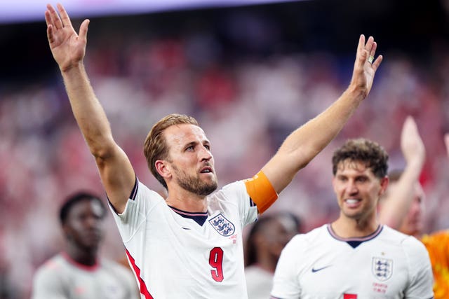 Harry Kane celebrating on the pitch in an England shirt, with both arms raised