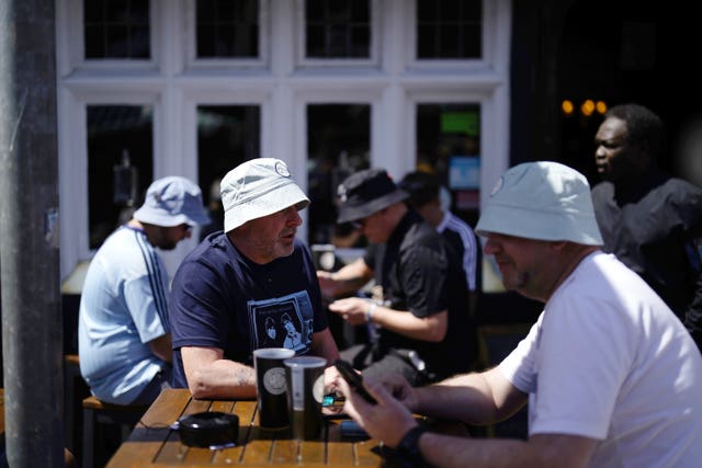 Oasis fans wearing bucket hats enjoying a pint in the Cardiff sunshine