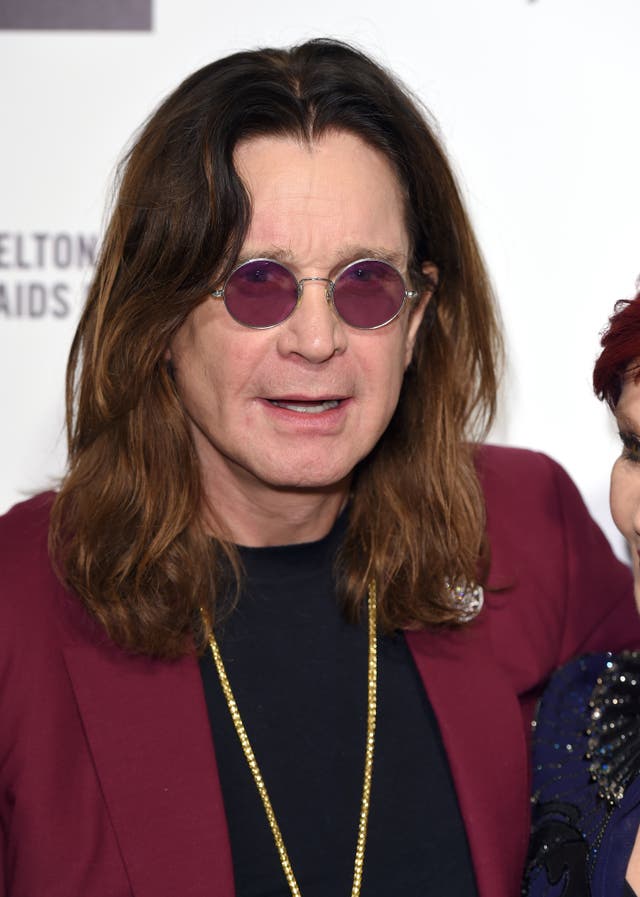 Ozzy Osbourne wearing red round-rimmed glasses and a suit