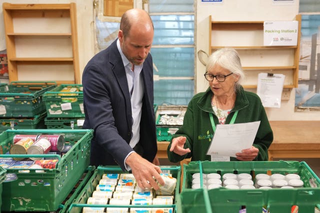 Prince of Wales looking at groceries while a woman speaks to him