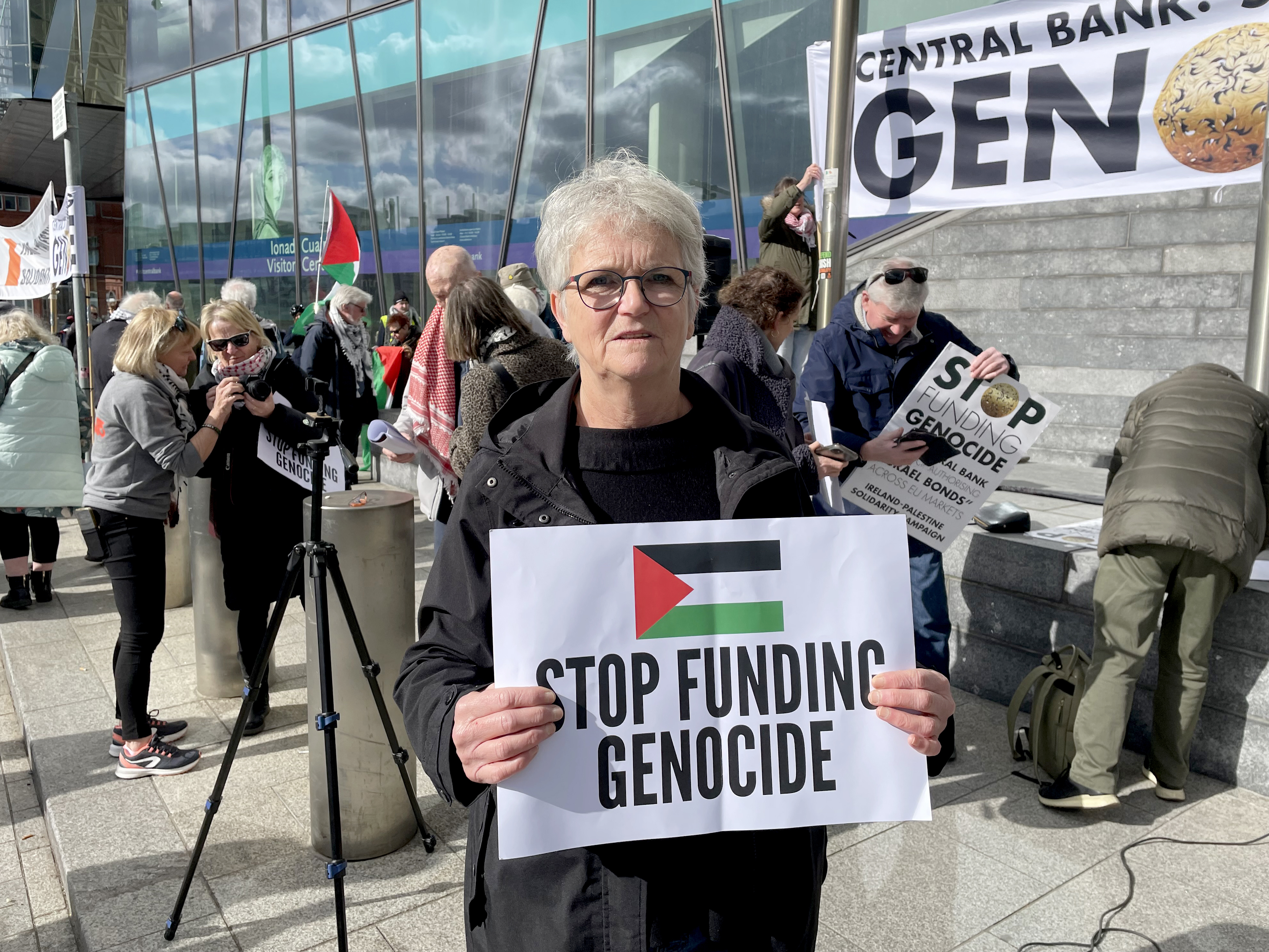 A woman holding a sign reading 'Stop funding geocide' amid a protest