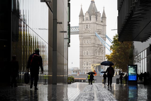 People use umbrellas during rain, with Tower Bridge visible in the background