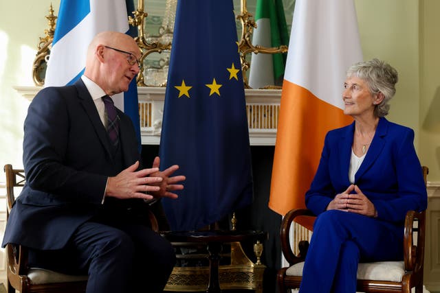 Catherine Connolly and John Swinney talking while seated beside each other, with Scottish, Irish and EU flags behind them