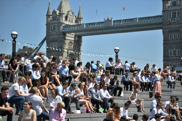 People enjoy their lunch break in the sunshine near Tower Bridge in London
