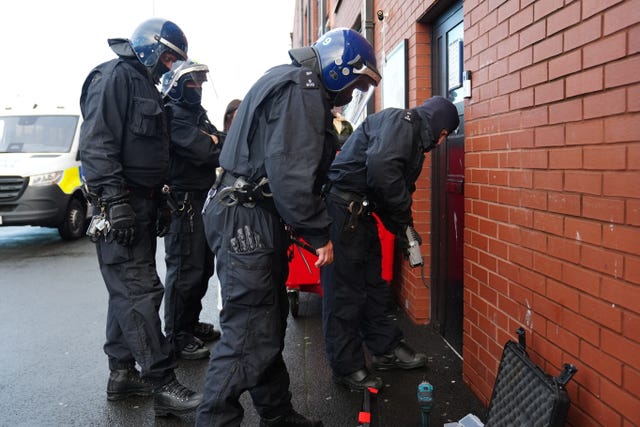 A group of police officers in protective helmets outside a door