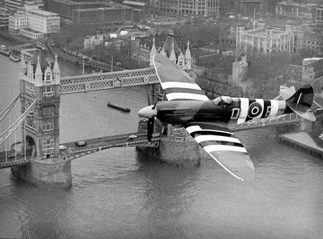 A Spitfire in Normandy invasion markings flying over Tower Bridge in London (David Jones/PA)