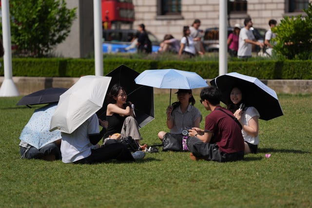 People sat under umbrellas in the sun in Parliament Square, London