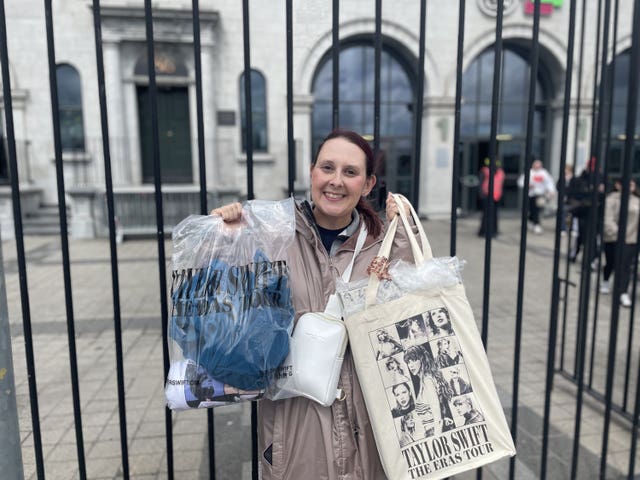 A woman standing in front of iron railings holds up two bags of merchandise