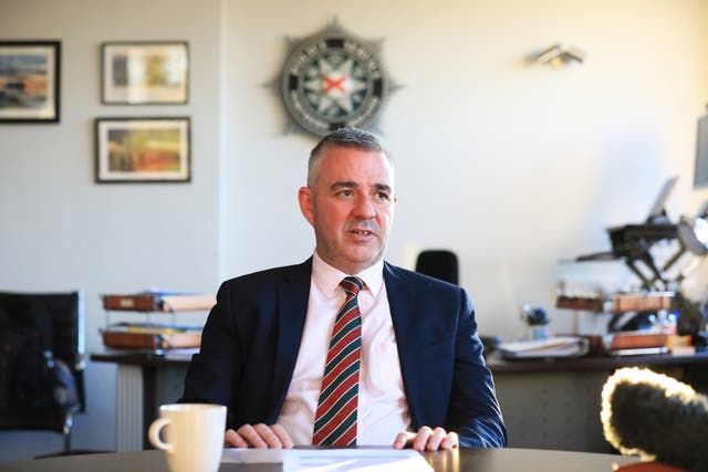 Liam Kelly seated at a desk, with a PSNI logo on the wall behind him