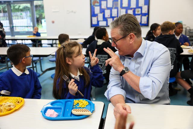 Sir Keir Starmer and a school girl gesturing towards each other as pupils sit down to eat their dinners