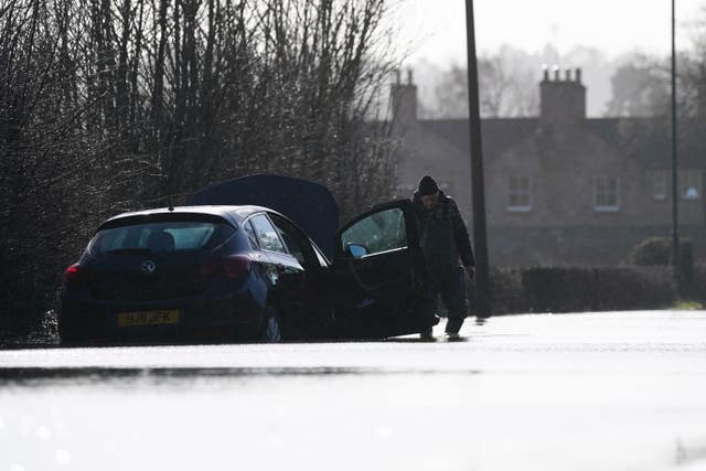 A man standing next to a car stranded in floodwater