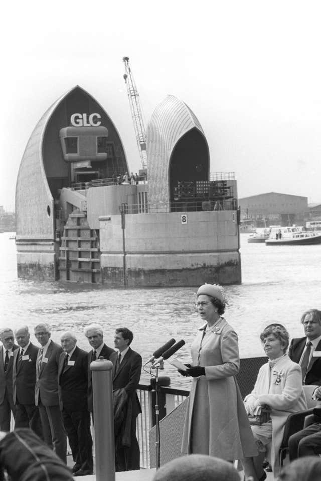 An image of the late Queen speaking on a stage in front of one of the iconic towers of the barrier