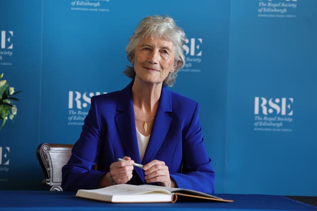 Catherine Connolly smiling while seated, holding a pen in front of RSE signage