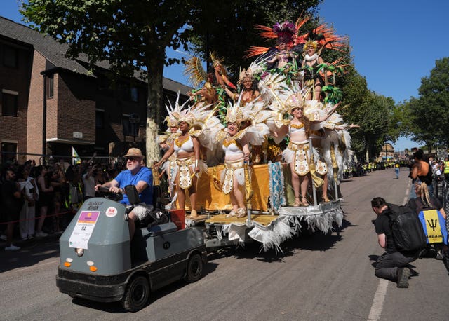 A man on a small grey vehicle pulls a float with lots of woman wearing white feathers